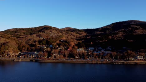 golden hour view of a serene lakeside town with autumnal trees and hillside homes, clear skies above