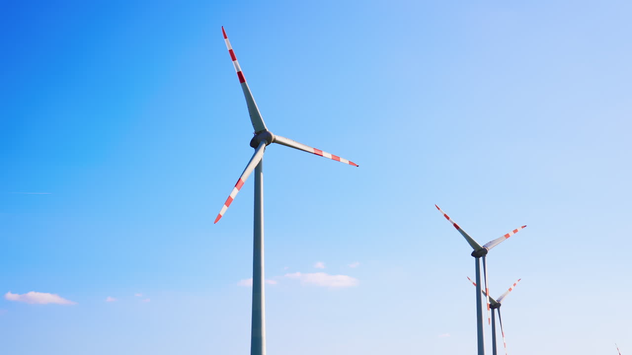 Wind turbines produce clean energy. Two large wind turbines spin against a clear blue sky, showcasing renewable energy production in a serene setting