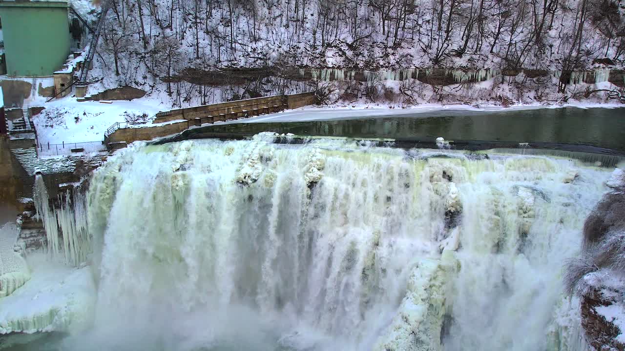 beauty of a powerfall cascading over icy cliffs in a stunning winter landscape, surronded by snow-covered forest