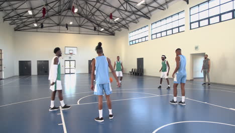 multiracial male basketball players playing basketball, coach observing in gym