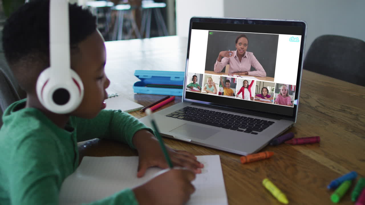 Schoolboy using laptop for online lesson at home, with diverse teacher and class on screen