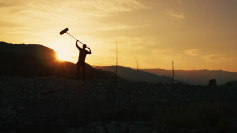 silhouette of film sound recordist is capturing background nature on the mountains