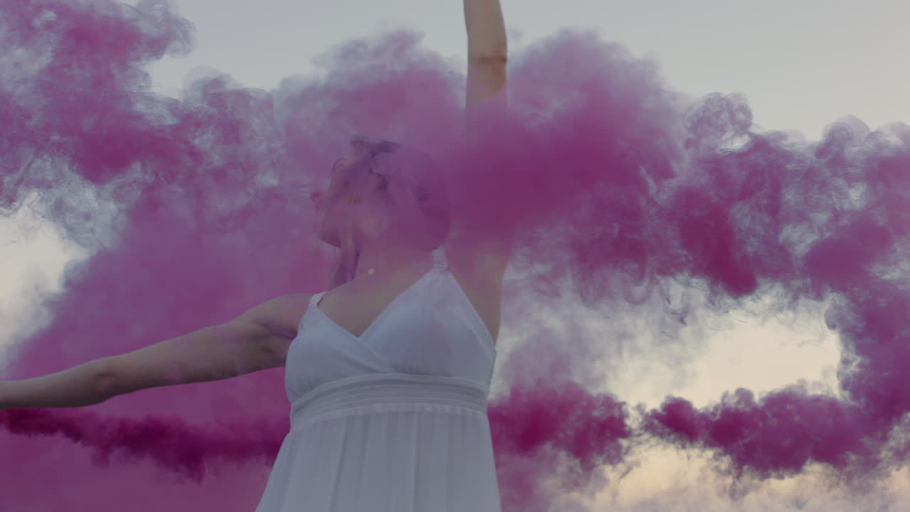 hermosa mujer agitando granada de humo rosa bailando en la playa temprano en la mañana celebrando la libertad creativa