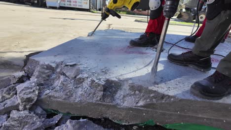three men on concrete block, two man using heavy-duty jackhammer tool and breaking reinforced concrete.concrete fly into pieces in slow motion.