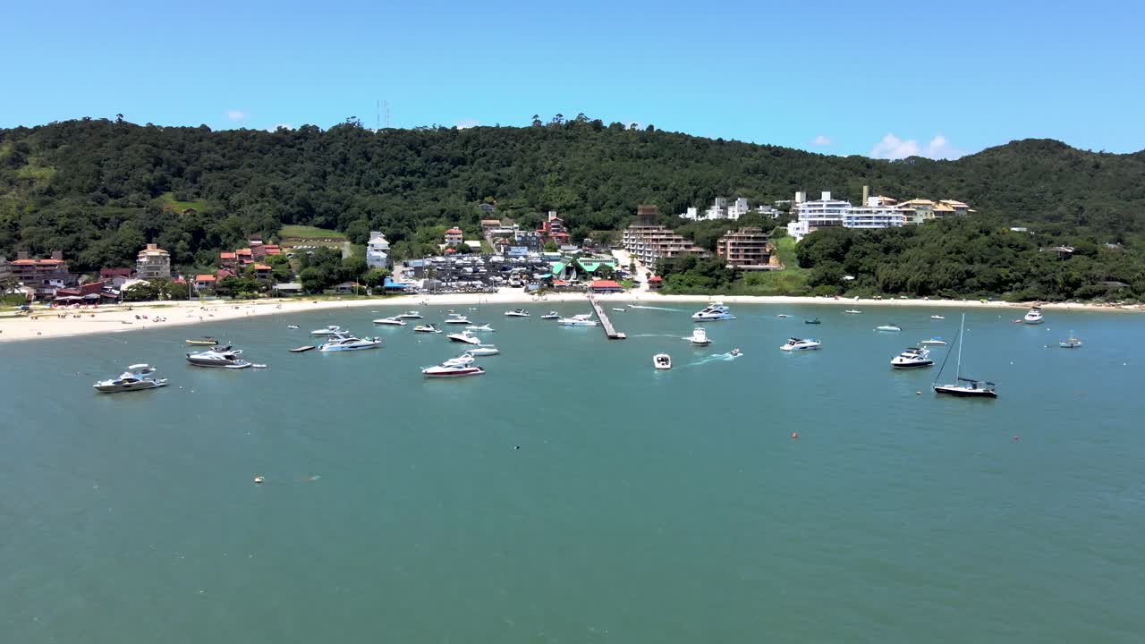 escena aérea de drones volando alto sobre lanchas rápidas, yates y barcos de lujo con muelle en playa paradisiaca en playa canajure florianópolis santa catarina