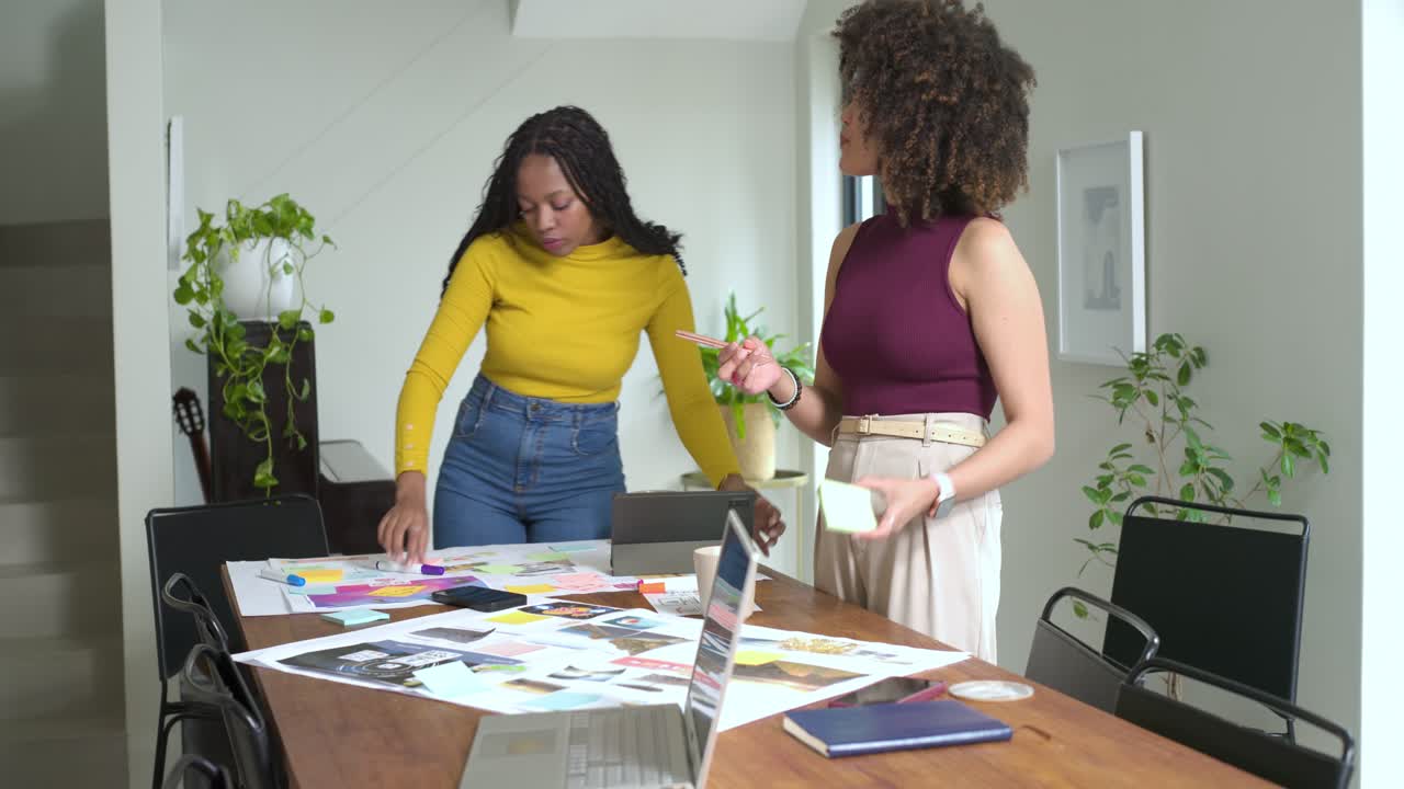 Using photos and notes, diverse female coworkers are arranging board at table and finalizing design
