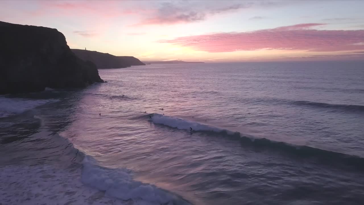силуэт скалы на фоне заходящего солнца и серфингистов, играющих в океане в корнуолле