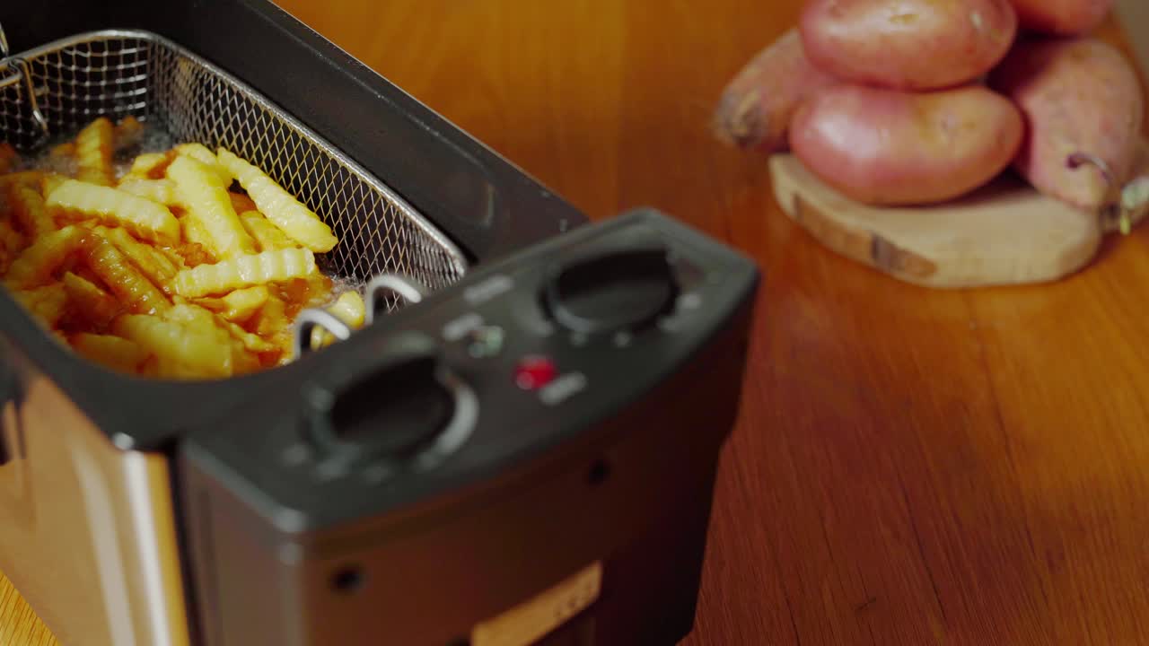 Nærbillede af elektrisk friturekoger, låget er åbent med stegende pomfritter