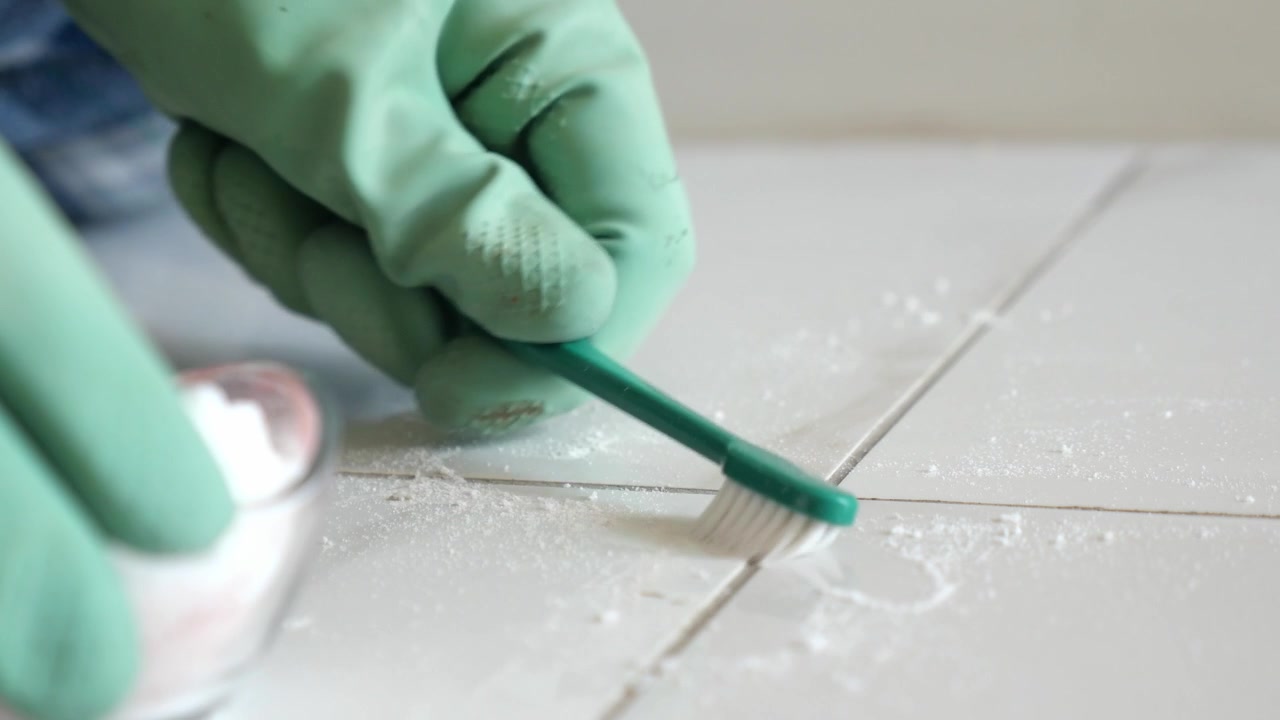 Person Scrubbing Tile Grout with Toothbrush and Cleaning Powder