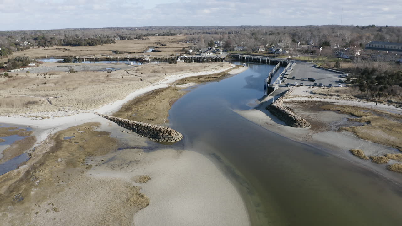 The camera pulls back to reveal the inlet or entrance to Rock Harbor in Orleans, Ma. The breakwater structures protect the entrance from large wakes. The tide is low and the water is calm.