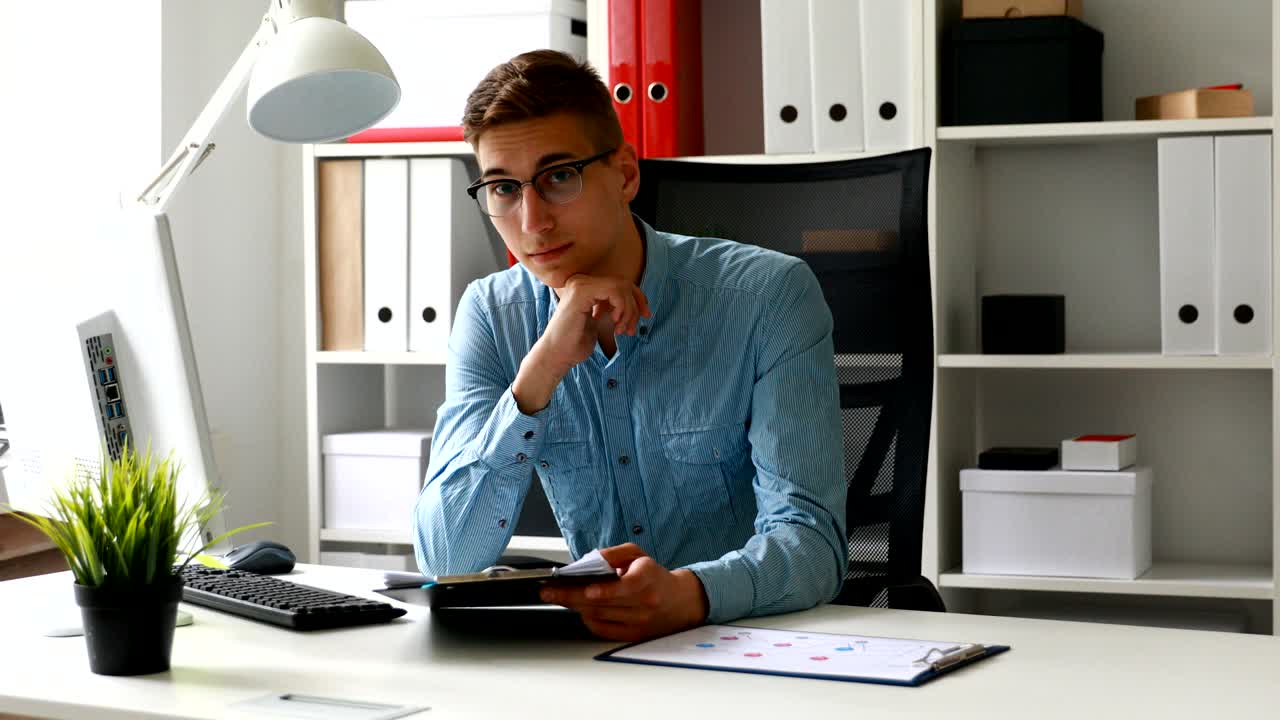 trabajador de oficina con gafas, sentado en la mesa y mirando a la cámara