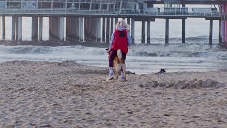 Una-Adiestradora-De-Perros-Entrena-Y-Camina-Con-Su-Perro-Pastor-De-Animales-En-La-Playa,-Estilo-Cinematográfico-En-Cámara-Lenta