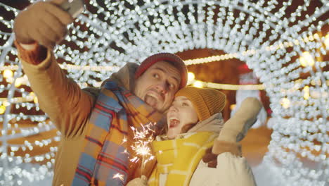 joyous couple taking selfie with christmas sparkler outdoors