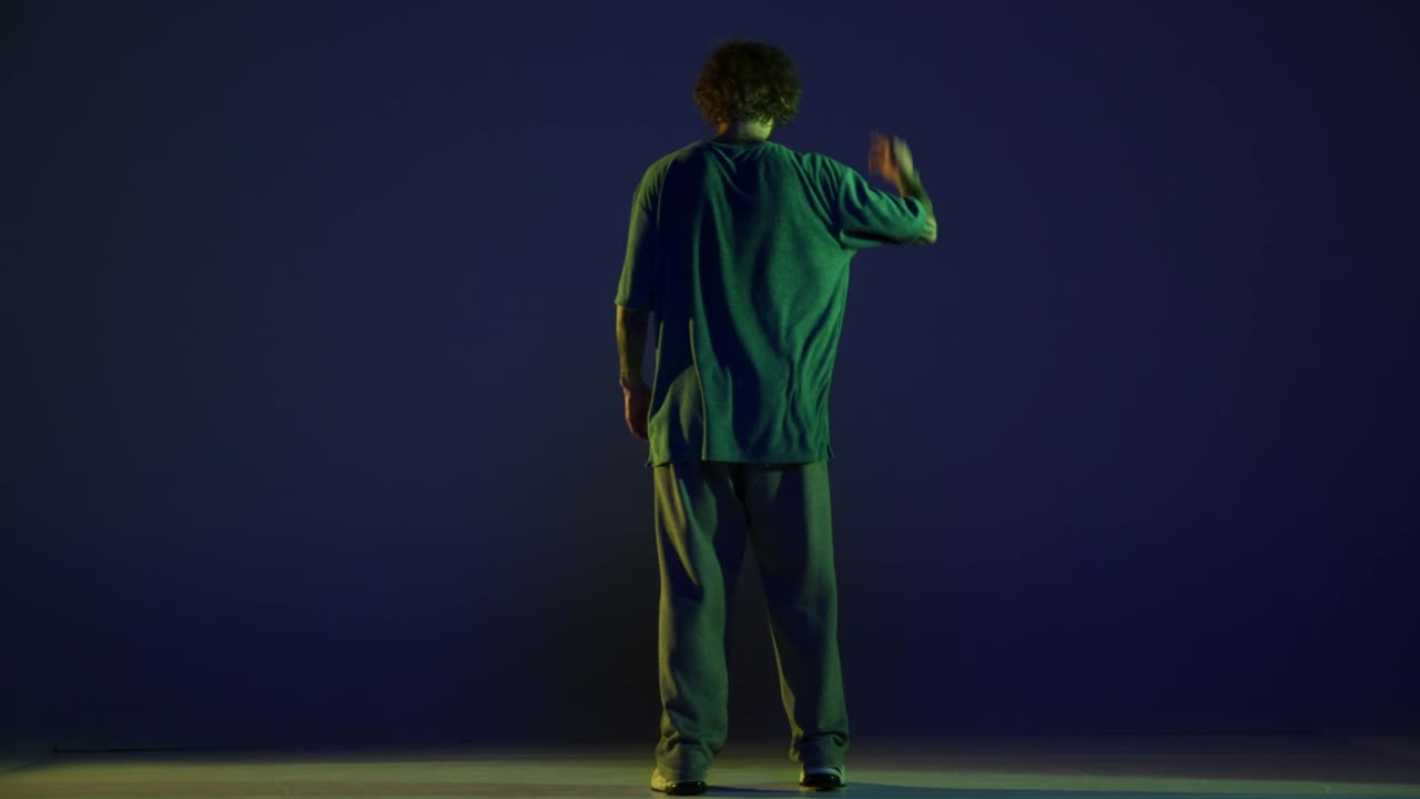 Energetic young man, hip-hop dancer dancing, running away isolated over dark blue background in neon light. Modern dance art, fashion, youth, ad, style. 4K, video