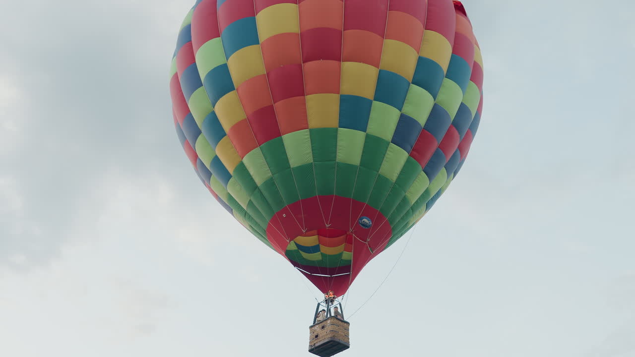 passengers riding colorful hot air balloon soaring over open field under soft sky gripping burner valve as flame bursts upward creating scenic aerial adventure in gentle evening breeze