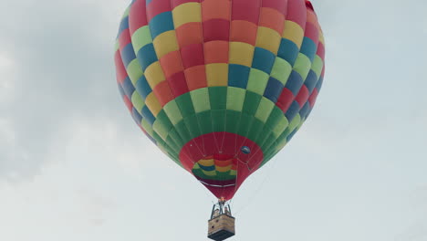 passengers riding colorful hot air balloon soaring over open field under soft sky gripping burner valve as flame bursts upward creating scenic aerial adventure in gentle evening breeze
