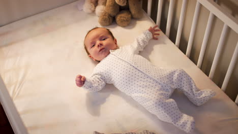 newborn baby boy lying on back in nursery cot at bedtime