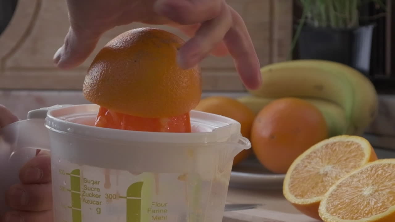 Mano exprimiendo jugo de naranja con un exprimidor de plástico para una bebida refrescante por la mañana