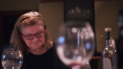 older woman with glasses sitting on dining table, looking at camera with smile. happy thoughtful senior female at family dinner