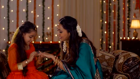 south-indian mother playing with her cute little daughter - sitting on the couch in traditional festive dress