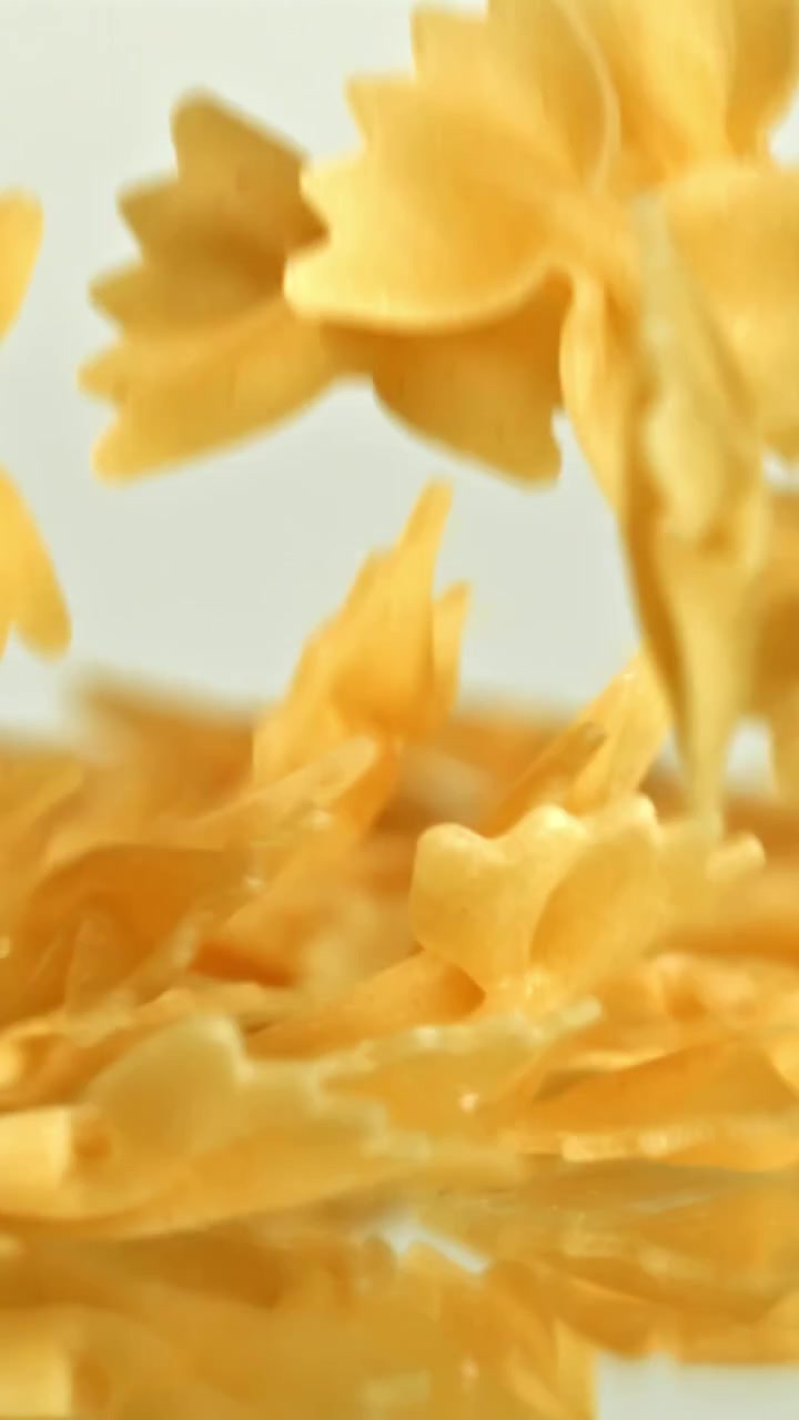 Pasta farfalle che cade al rallentatore su sfondo bianco.