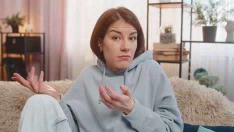 confused caucasian woman on sofa raising eyebrows feeling embarrassed about ambiguous question