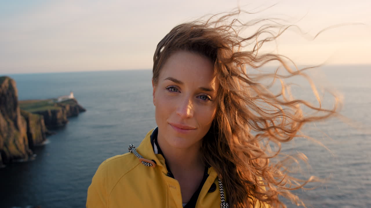 Donna con i capelli ricci su una scogliera a picco sull'oceano al tramonto