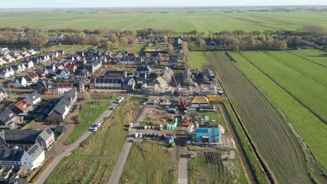 Antenne-Der-Baustelle-In-Einem-Neu-Gebauten-Vorort,-Umgeben-Von-Grünen-Wiesen---Rückwärts-Fliegende-Drohne