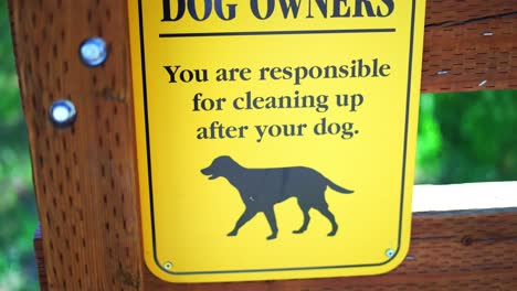 notice to dog owners you are responsible for cleaning up after your pet bright yellow sign at public national park hiking trail, panning from top to bottom, in 4k slow motion