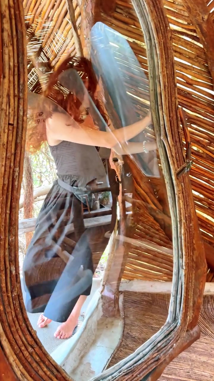 Donna in piedi davanti a uno specchio all'interno di un edificio rustico. Una donna sta accanto a uno specchio all'interno di un edificio fatto di legno e materiali naturali in Messico