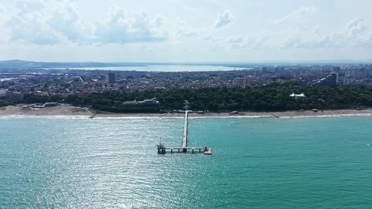 Vista di un lungo molo che si estende nell'oceano vicino a una città costiera in una giornata limpida con nuvole sparse.