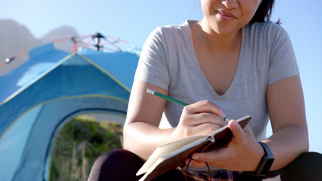 writing in notepad, woman sitting near tent during mountain hike