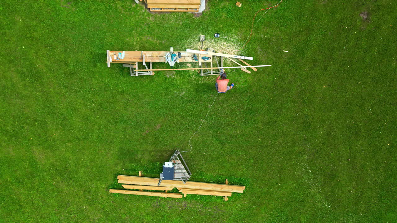 A Man Working on Assembling Wooden Pieces on a Grassy Area - Aerial Topdown Shot