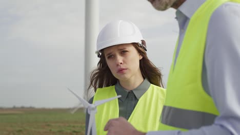 team of caucasian engineers standing on wind turbine field and discussing over project.