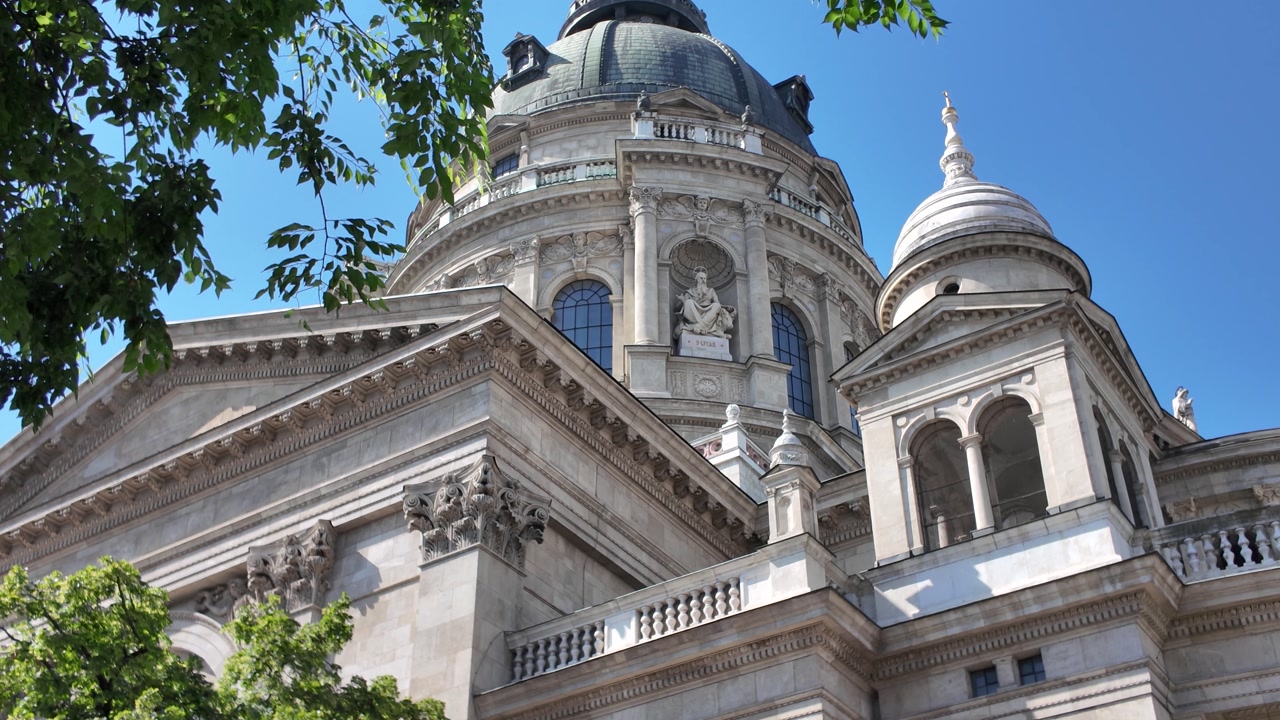 Iconic dome of St. Stephen’s Basilica in Budapest, with tree foliage in the foreground, highlighting historic elegance