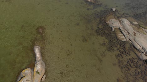 Drone-Volando-Sobre-La-Vista-A-Través-De-Agua-Verde,-Océano,-Con-Rocas-Y-Un-Pequeño-Puente