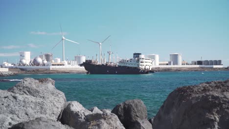 abandoned ship in industrial harbor with wind turbines