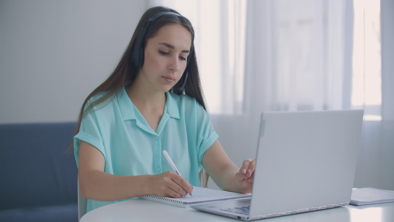 mujer estudiante sentarse en el escritorio en casa usar auriculares hablar a distancia por video llamada aplicación y dispositivo portátil e-aprender idiomas estudiar con e tutor o compañero de clase hacer tarea común remotamente concepto de tecnología moderna