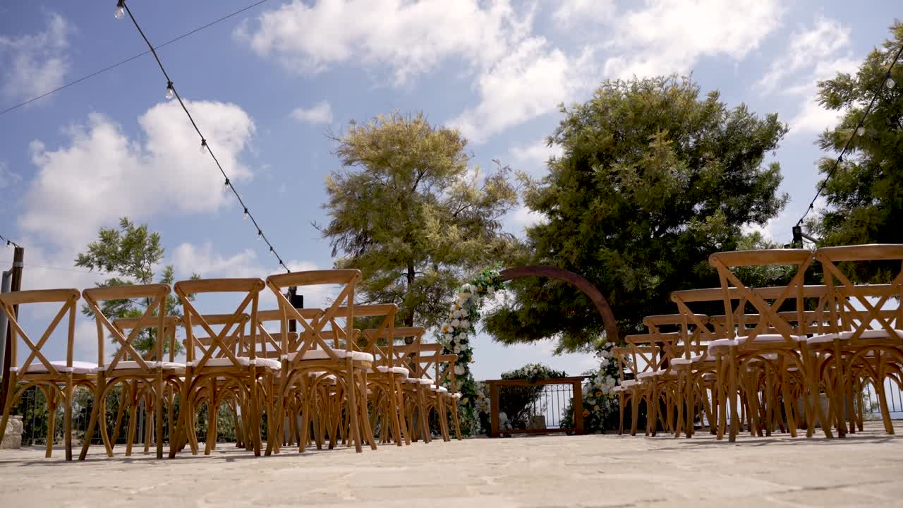 Outdoor dining setup with wooden chairs under blue sky and trees in a quaint location