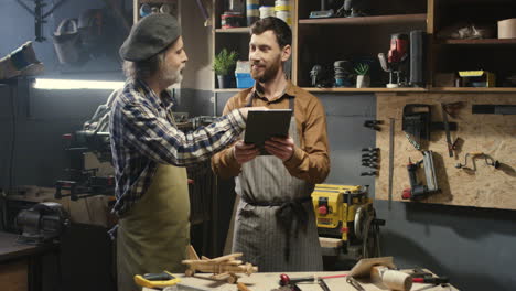 two carpenters standing in workshop and watching some video on tablet in carpentry workshop