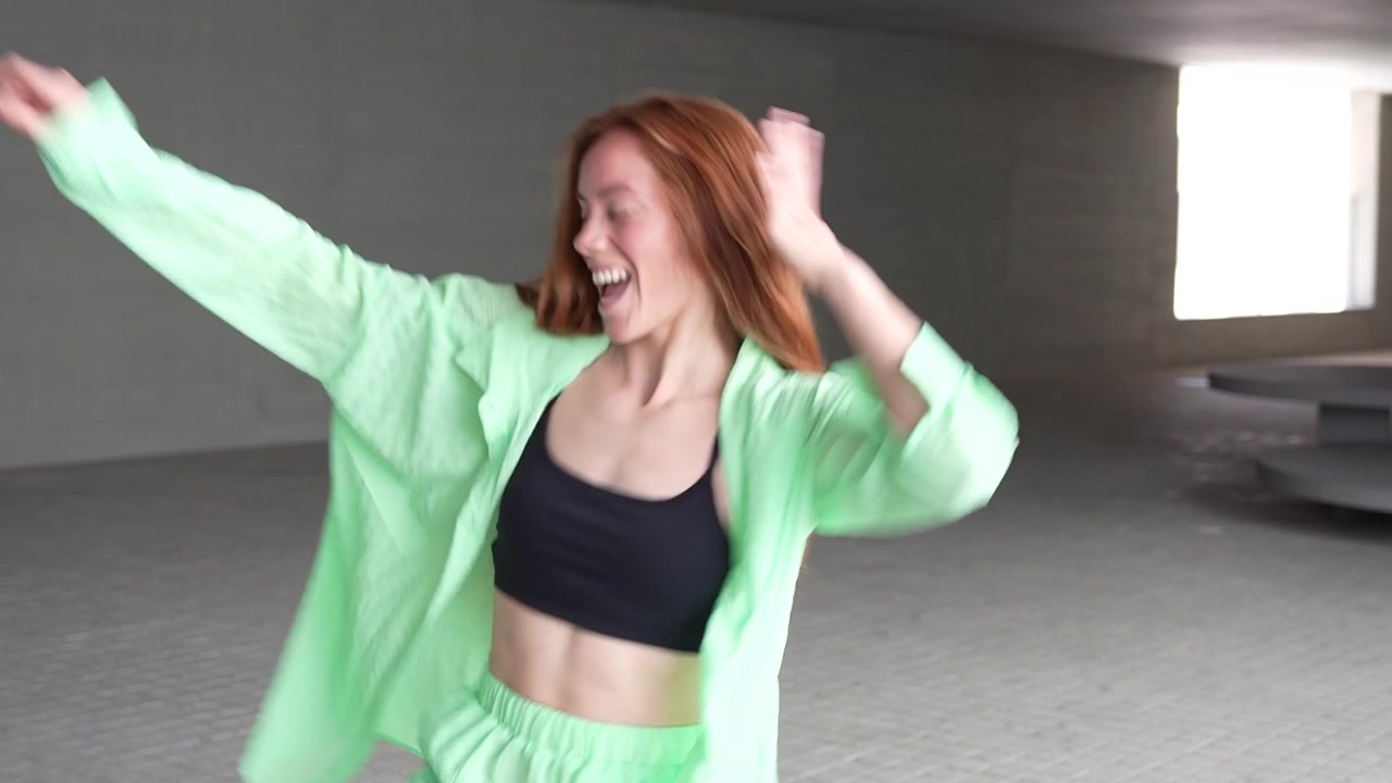 A woman energetically dances in a green outfit in a city showcasing expressive choreography