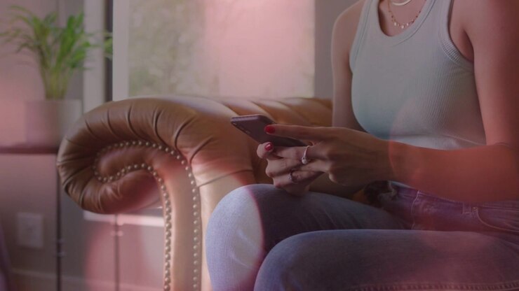 Woman tapping and scrolling smartphone on sofa, pink overlay highlighting mobile UI during browsing