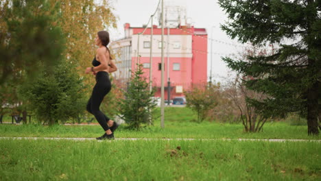 background with dry trees and building while lady runs on street, vibrant greenery and urban backdrop creating dynamic scene of woman running through city park path