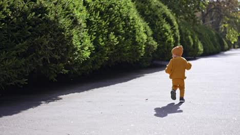 catching up with a kid wearing yellow clothes and cap. toddler runs by the alley in the park.