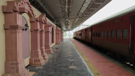 view of vadnagar station in gujarat, india, red train on track and cooling fans on platform roof.