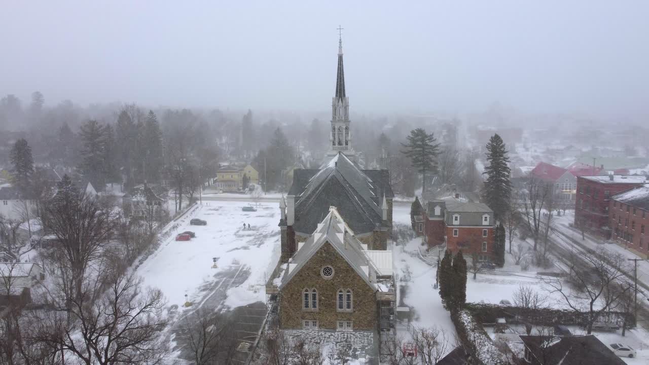 Orford Quebec Canada winter snow falling over city church building, aerial drone