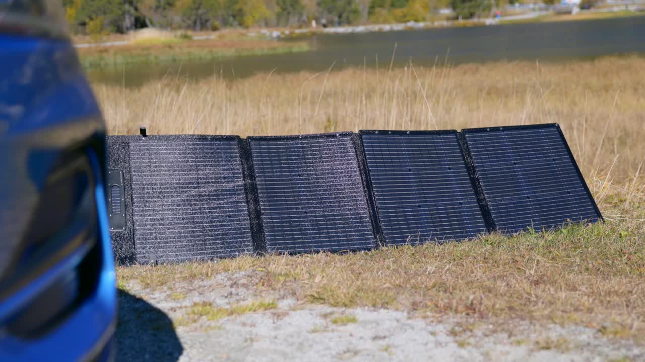 Portable solar panels are laid out on a grass field outdoors near a lake providing renewable energy and sustainable power generation solutions