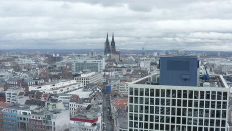 Aerial-descending-footage-of-large-city.-Revealing-modern-office-building-with-glossy-windows-reflecting-surrounding-buildings.-Cologne,-Germany