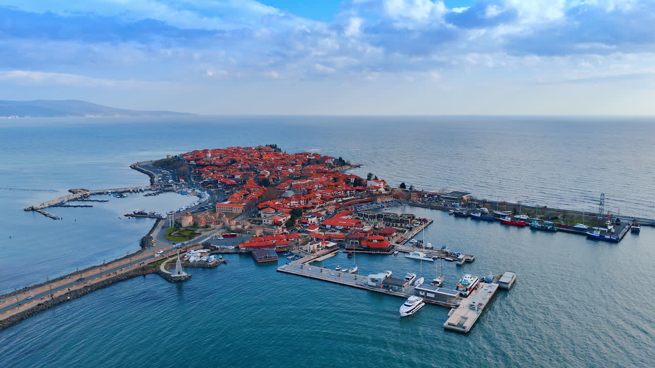 Kustvy över en liten stad vid havet. Flygfoto visar en liten stad nära kusten med båtar och bryggor. Vatten omger staden under en blå himmel.