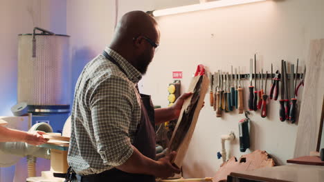 man in woodworking shop inspecting lumber piece before assembling furniture